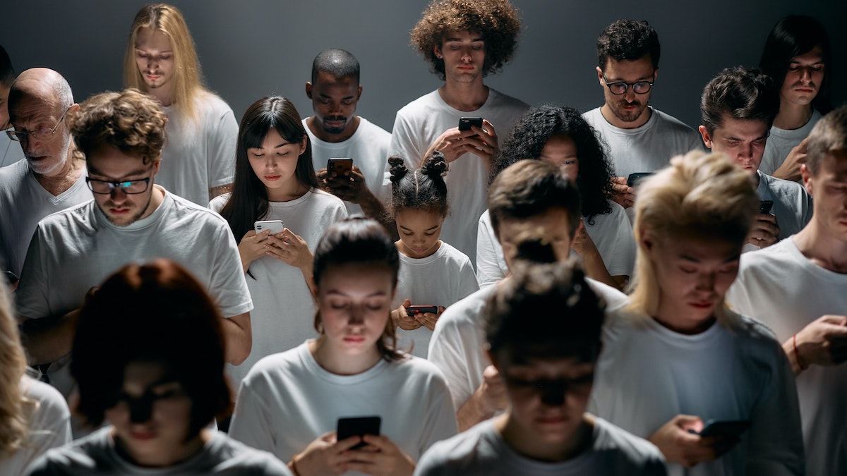 Redes que atrapan: multitud de personas de diferentes edades y razas mirando su teléfono móvil