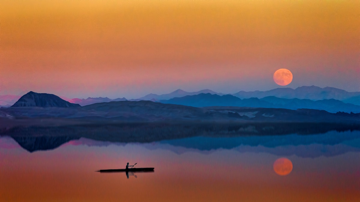 ¿Está tu nombre escrito en los cielos? Persona rema kayak en lago tranquilo al lado de las montañas justo al atardecer con una luna llena enorme.