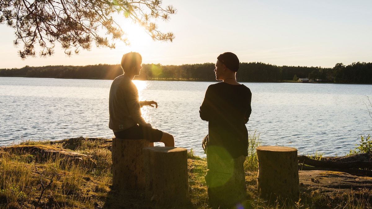 miedo a evangelizar: dos hombres jovenes sentados en troncos al lado de un lago hablando al atardecer