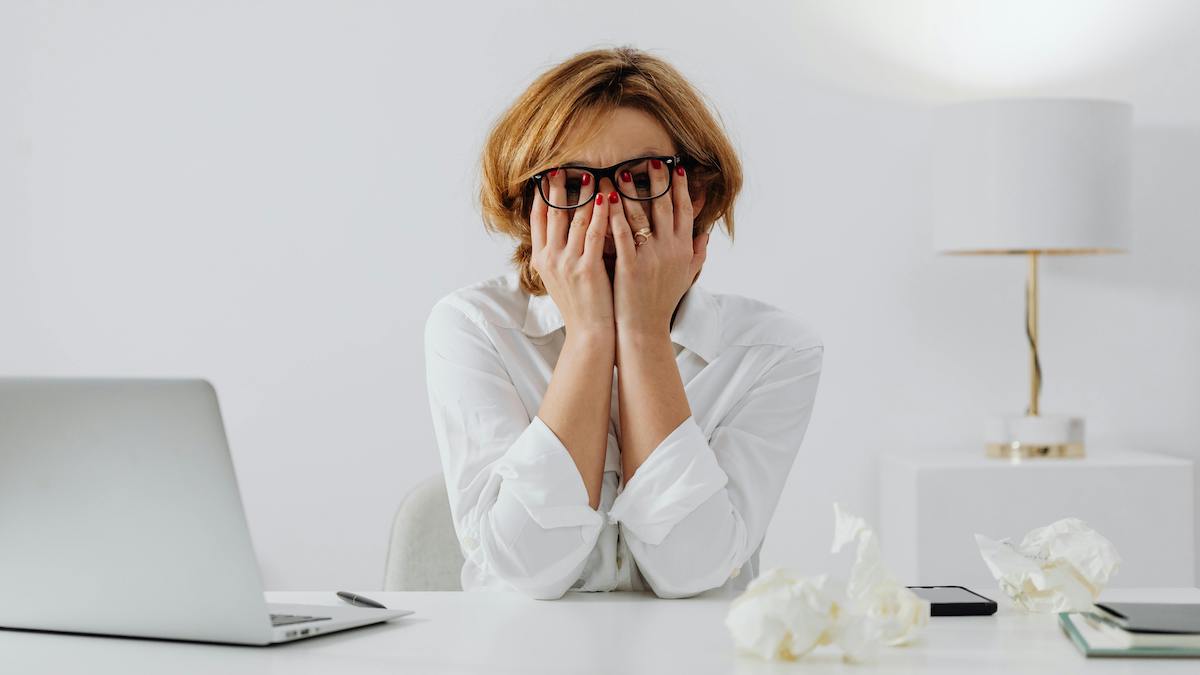 Antídoto a la ansiedad y el cansancio: Mateo 11:28-30. Mujer estresada al lado de un portátil en un despacho blanco.