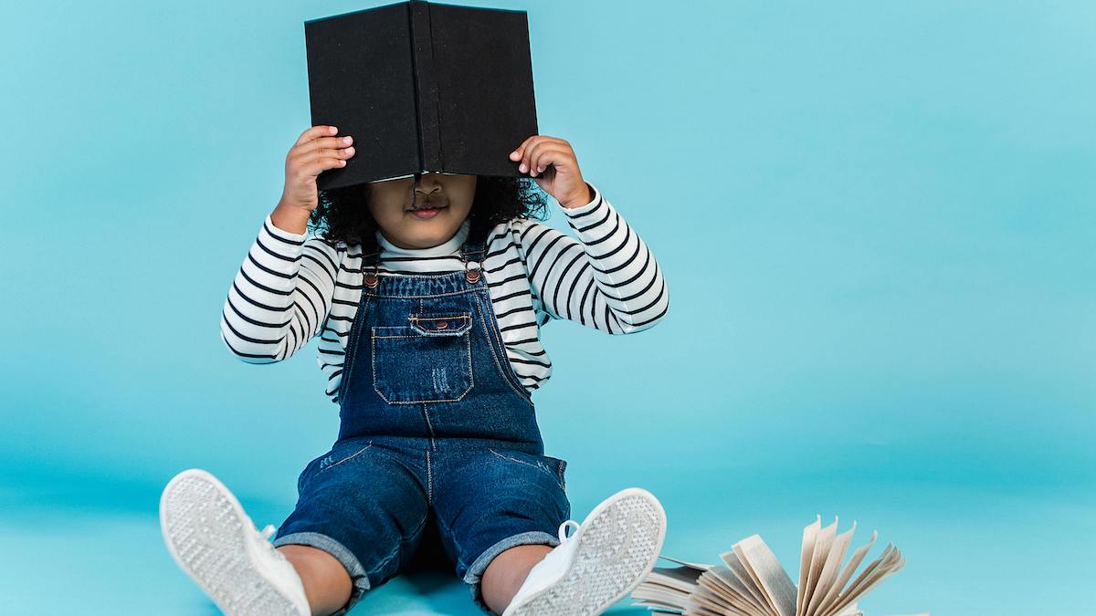 niña en infantil sostiene libro negro en alto tapándole la cara para blog sobre no tengo tiempo para leer 7 soluciones
