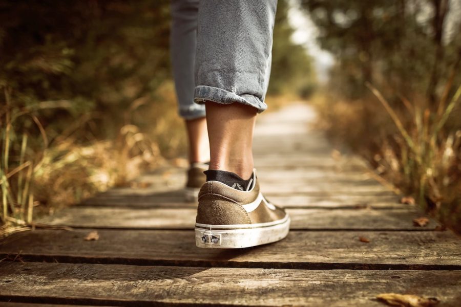 Caminar con Jesús: foto de las piernas en vaqueros o jeans desde atrás, con zapatillas de deporte marrones, caminando por una senda hecha de tablones de madera