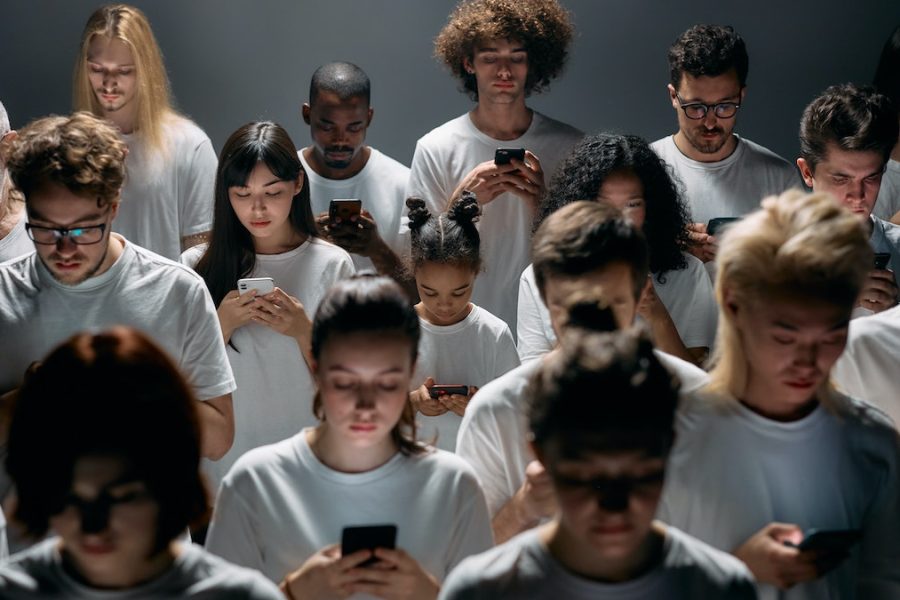 Redes que atrapan: multitud de personas de diferentes edades y razas mirando su teléfono móvil