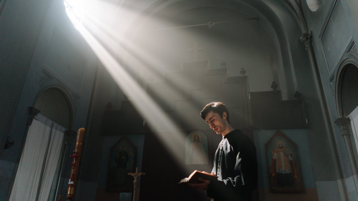 Día de la Reforma Protestante: un joven vestido de negro lee una Biblia en una iglesia, iluminado por los rayos de luz que penetran por una ventana
