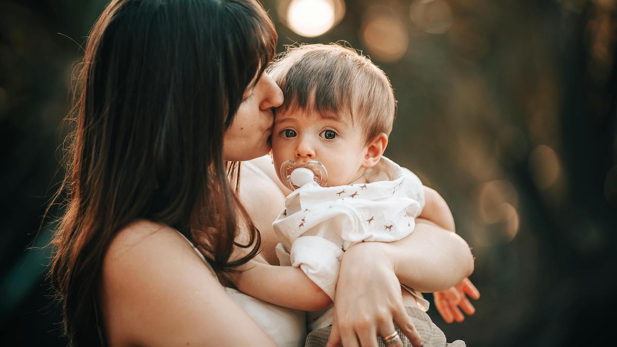 joven madre con pelo castaño abraza a un bebé con chupete para blog devocional sobre cinco cosas que toda madre cristiana debe saber