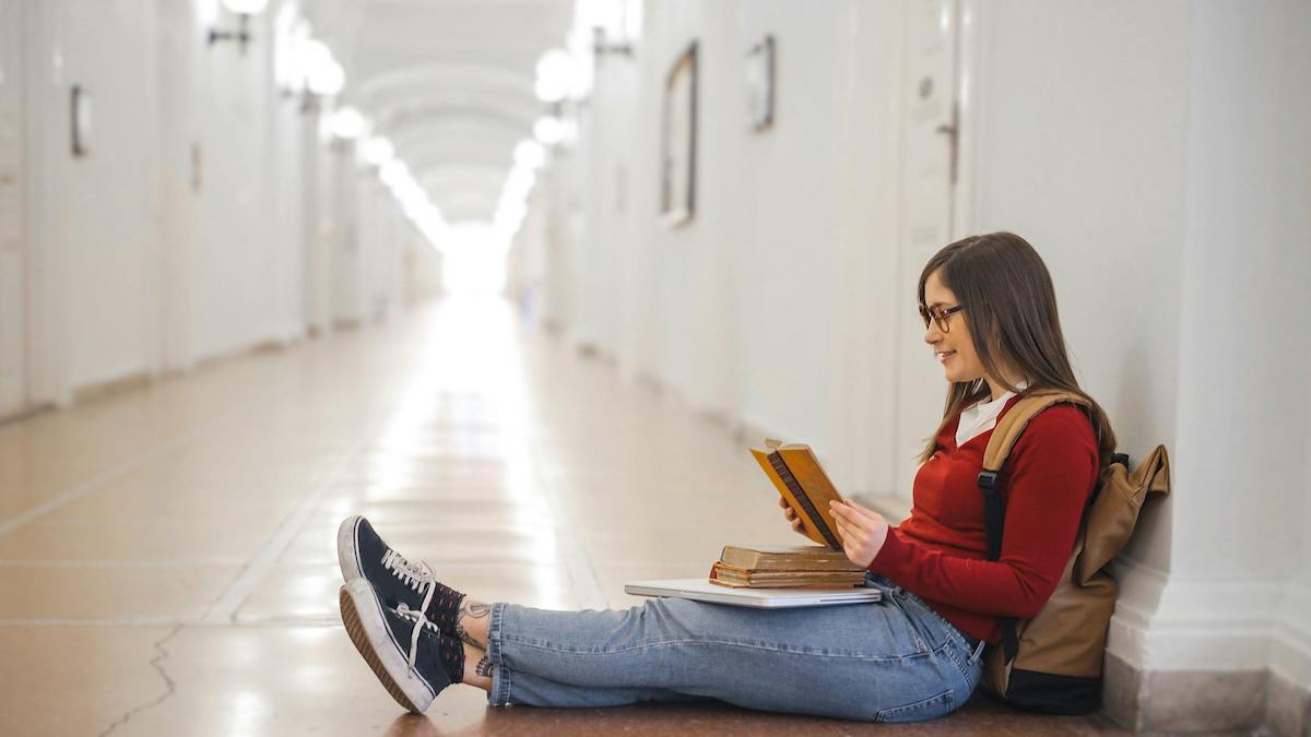 chica con jersey rojo leyendo en el suelo de un pasillo para ilustrar blog sobre los beneficios de la lectura